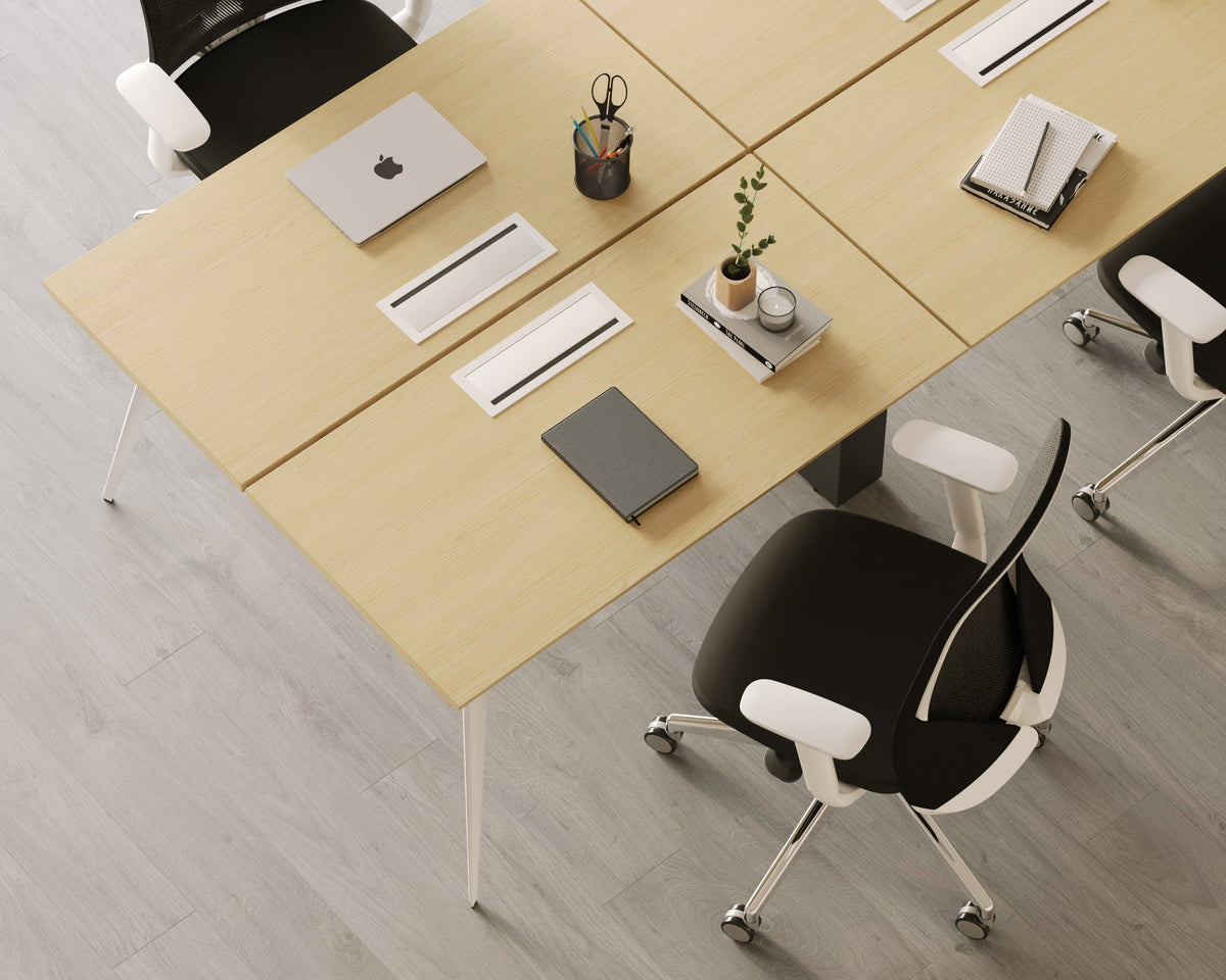 Light Oak Urbanica workstation table on a white frame with cable cutouts in the top and black mesh office chairs pulled up to it, seen from above