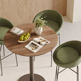 Close-up of round walnut bistro small tabletop with vase, books, and green apples, surrounded by green stools