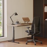 Home office desk setup with adjustable laptop stand in walnut finish, ergonomic chair, desk lamp, and books.