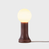 Shore table lamp with mouth-blown recycled glass base and glowing matte bulb, shown against a light grey background with visible fabric cord.
