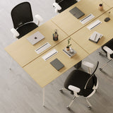 Top-down close-up of Urbanica six person office workstation desk showcasing natural wood grain surface, integrated power outlets, and modern black mesh chairs with white armrests