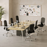 Urbanica six person office workstation desk setup in a modern workspace featuring a light wood collaborative table and six ergonomic black mesh swivel chairs on casters