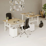 Urbanica Two-Person Standing Office Desk with height-adjustable legs, modern dual workstation setup, and sleek ergonomic chairs in a collaborative workspace