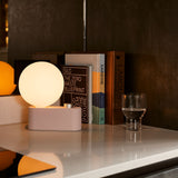 Alumina Lamp in Blossom finish used as a desk light, placed beside books and a glass of water on a modern countertop.