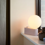 Alumina Lamp in Blossom finish placed on a window ledge, softly illuminating a modern living space.