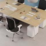 Close-up of the Urbanica Quad Office Workstation Desk showcasing a warm wood finish, functional cable cutouts, and a collaborative 4-person layout with ergonomic chairs and modern storage drawers.