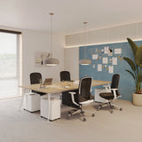 Urbanica Quad Office Workstation Desk featured in a stylish, collaborative office setting with four mesh chairs, organized workstations, moodboard wall, and natural lighting—perfect for modern team environments.